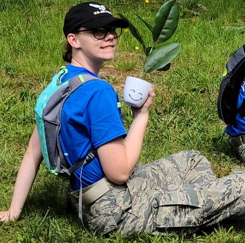 Cadet sitting on the ground holding her team's potted plant